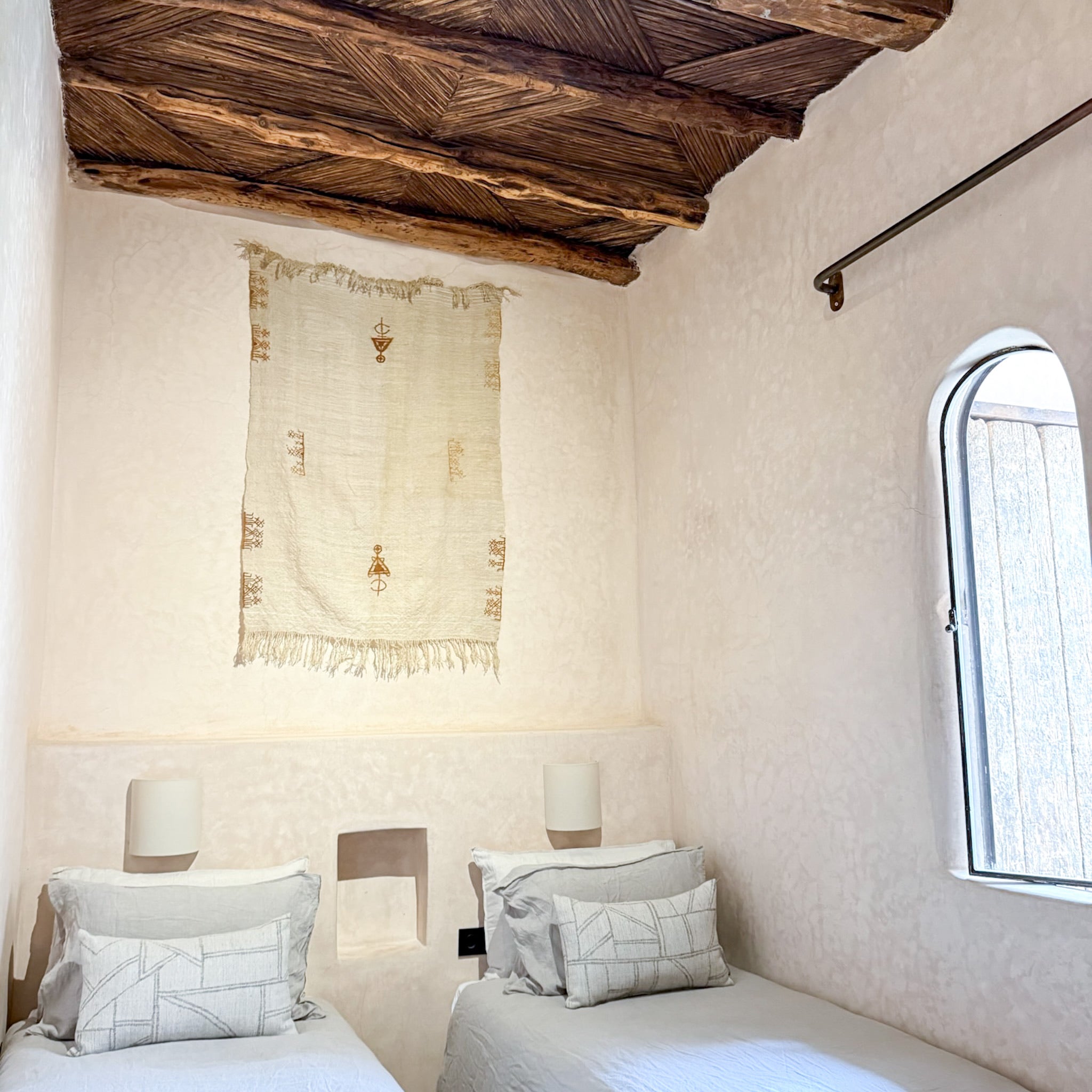 Cozy bedroom with wooden ceiling, arched window, and two beds.
